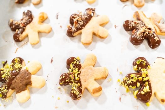 Crafting star-shaped holiday cookies dipped in chocolate and sprinkled with crushed pistachios, arranged on parchment paper.