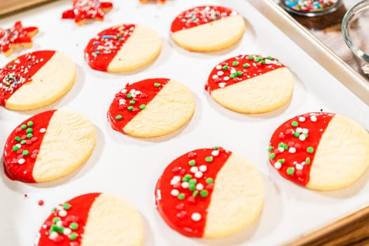Skillfully decorating cookies with vibrant red melted chocolate and a generous sprinkle of vibrant green, creating a festive holiday treat.