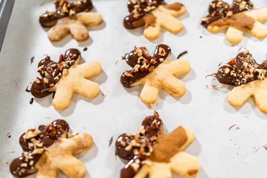 Creating snowflake-shaped cutout sugar cookies, dipped in chocolate, and adorned with crushed pecan nuts, elegantly presented on parchment.