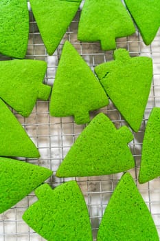 A cooling rack filled with freshly baked Green Gingerbread Cookies in Christmas tree shapes, displaying a vibrant green color that contrasts against the silver rack.