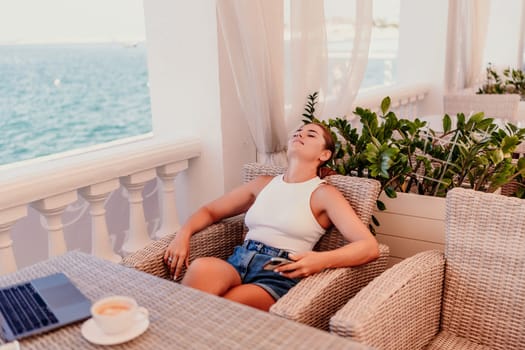 woman is sitting at a table with a laptop and a cup of coffee. She is wearing sunglasses and a ponytail. The scene suggests a relaxed and leisurely atmosphere