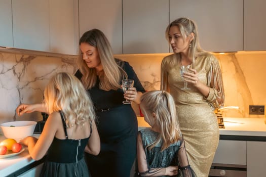 Four women and two girls gather in a modern kitchen. Two girls bake, while the women watch and hold drinks. Warm lighting illuminates the scene.