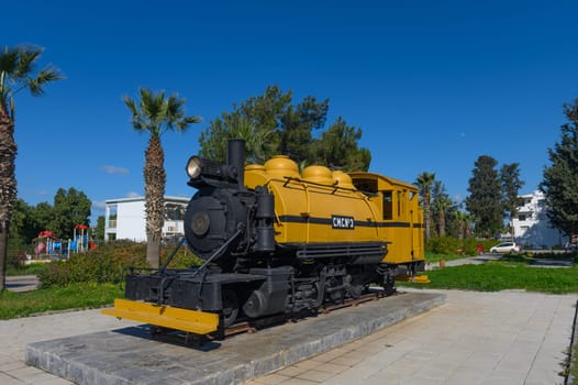 A charming yellow locomotive stands proudly in a park, surrounded by palm trees and bright playground equipment.