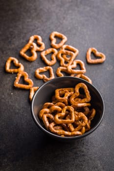 Heart shaped pretzel in bowl on a black table.