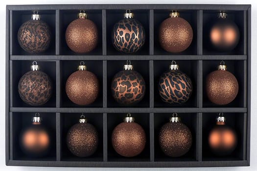 A beautifully organized display of bronze ornaments in various textures and patterns sits in a black storage box. This festive arrangement adds a touch of elegance to seasonal decor.