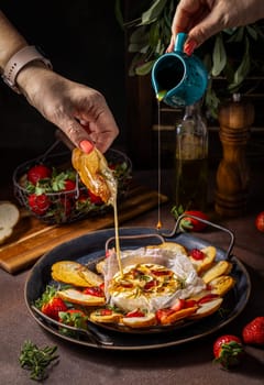 Chef pouring honey over a delicious baked camembert cheese with strawberries and toasted bread, a perfect appetizer for sharing