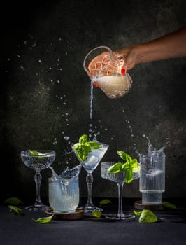 Bartender pours a drink into a cocktail glass, creating a splash and surrounded by other glasses with basil and ice