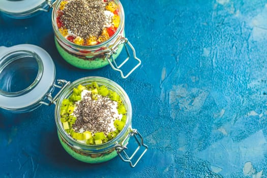 Two glass jars brimming with vibrant green chia seed pudding, layered with yogurt and topped with fresh kiwi and mango