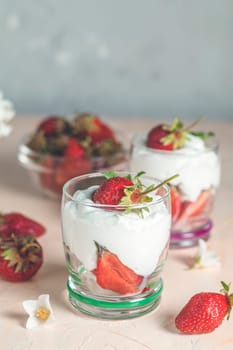 Two glasses with layered dessert of strawberries and cream cheese decorated with fresh strawberries and jasmine flowers on pink background