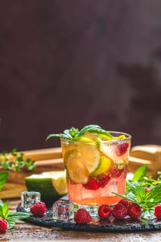 Glass of vibrant pink raspberry lemonade infused with citrus fruits, ice, and fresh mint, creating a refreshing summer beverage