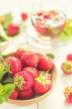 Ripe strawberries and fragrant mint leaves arranged in a wooden bowl, paired with a refreshing glass of strawberry tea, embodying summer