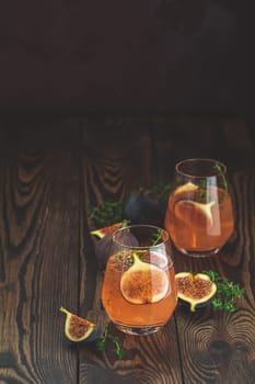 Two refreshing pink cocktails garnished with fresh figs and thyme sprigs sit on a dark wooden table, creating a vibrant and inviting scene