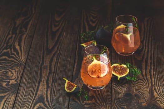 Two refreshing pink cocktails garnished with fresh figs and thyme sprigs sit on a rustic wooden table, creating a vibrant and inviting scene