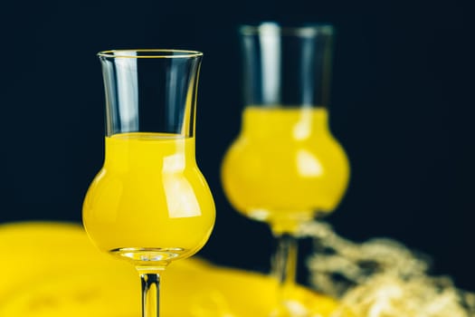 Two glasses filled with yellow liquor stand on a table with a dark background, creating a vibrant and inviting scene