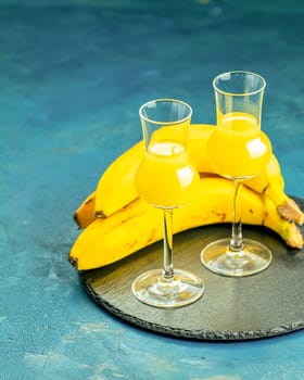 Two elegant glasses filled with vibrant banana liqueur sit on a slate serving tray alongside ripe bananas, creating a sophisticated and tropical presentation