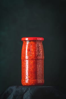 Glass jar full of traditional balkan vegetable spread ajvar or pindjur, with drops of condensation on glass, on black background