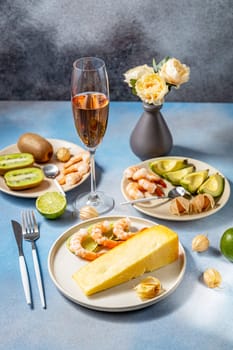 Elegant table setting with cheese, shrimp, kiwi, avocado, lime, and a glass of sparkling rose wine, creating a luxurious dining experience