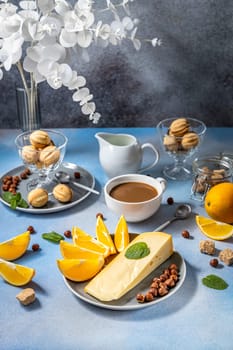 Enjoying a healthy and delicious breakfast with coffee, cheese, orange slices, nuts, and cookies on a blue table