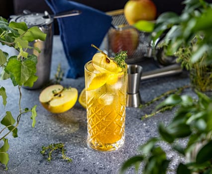 Golden apple cider cocktail in a crystal glass, garnished with fresh apple slices, lemon, thyme sprigs, and ice cubes