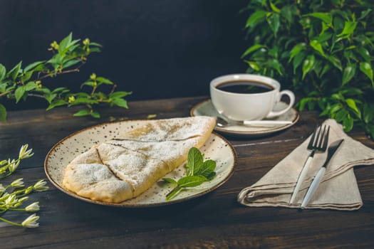 Delicious apple pie sprinkled with powdered sugar served with a cup of black coffee on a wooden table, creating a cozy and inviting atmosphere