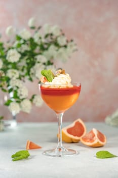 Layered grapefruit and orange jelly dessert in a coupe glass, topped with whipped cream, mint, and pistachio, accented by fresh grapefruit slices