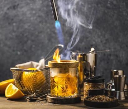 Bartender smoking a cocktail in an elegant glass with orange slices and bar equipment creating a visually appealing drink