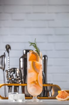 Pink grapefruit cocktail with ice cubes and rosemary, ready to be served on a bar counter with barman tools