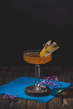 Refreshing cocktail garnished with pear slices and delicate flowers, served in a stylish glass on a dark wooden table with a blue napkin