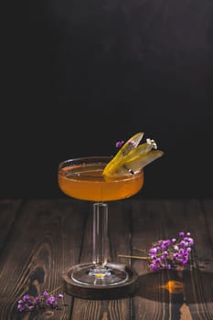 Pear cocktail garnished with pear slices and small flowers, served in an elegant coupe glass on a rustic wooden table