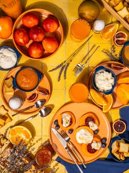 Colorful brunch table setting with various dishes, fresh fruits, yogurt, and citrus, creating a vibrant and inviting scene