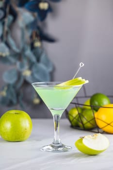Green apple cocktail served in a martini glass, garnished with thin slices of fresh green apple, accompanied by fresh fruit