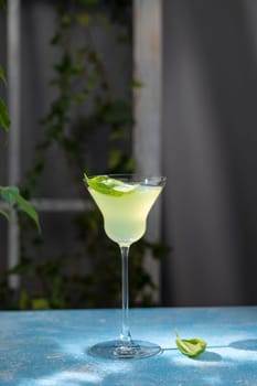 Refreshing yellow cocktail garnished with fresh basil leaves, served in an elegant glass on a vibrant blue table, creating a stylish and inviting summer drink presentation