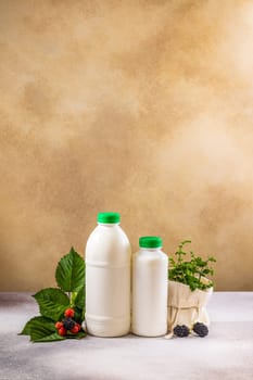 Arranging two white plastic bottles with green caps filled with milk or yogurt alongside fresh mint leaves and berries on a textured table