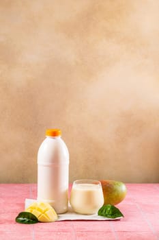 Refreshing mango lassi beverage alongside its ingredients, including a bottle of yogurt and fresh mango slices, creates a vibrant and tropical scene