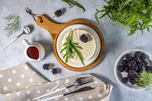 Top view of fresh round cheese with blackberries and rocket salad on wooden board, served with berry sauce, healthy eating concept