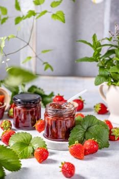 Two glass jars filled with homemade strawberry jam, accompanied by fresh strawberries, leaves, and a spoon, creating a vibrant and appetizing scene