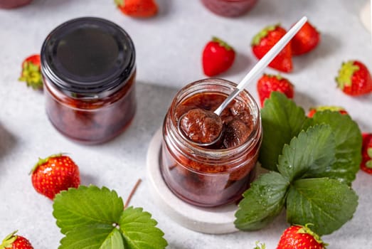 Glass jars filled with homemade strawberry jam, accompanied by fresh strawberries and vibrant green leaves, creating a delightful and appetizing scene