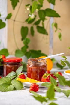 Glass jar with delicious homemade strawberry jam, decorated with orange slices and fresh strawberries