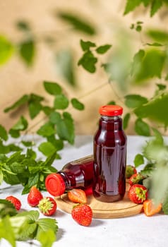 Two bottles of strawberry juice sit on a wooden coaster, surrounded by fresh strawberries and mint leaves, creating a refreshing summer scene