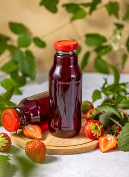 Two bottles of strawberry juice are standing on a wooden board with fresh strawberries and leaves, creating a refreshing summer scene