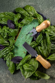 Green pesto gouda cheese is presented on a dark background with fresh basil leaves and serving cutlery, creating an appetizing display