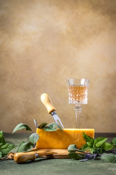 Block of mature cheddar cheese served with fresh herbs and glass of rose wine on a wooden board