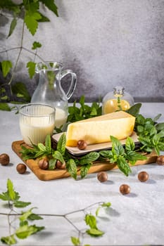 Hard cheese, milk, macadamia nuts, and mint leaves are arranged on a wooden board, creating a visually appealing and flavorful composition