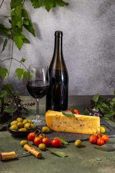 Arranging a bottle and glass of red wine with cheese, olives, cherry tomatoes, and basil leaves on a rustic table