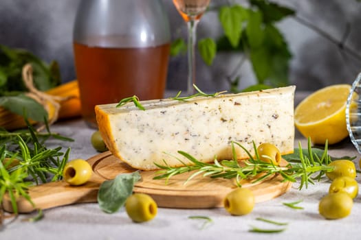 Close-up of delicious herb cheese with fresh rosemary and green olives, accompanied by a bottle of wine and a lemon, creating an inviting appetizer setting