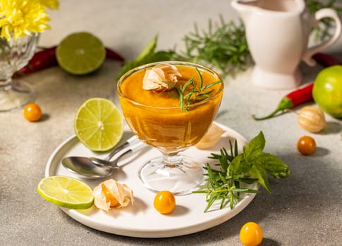 Glass cup containing a vibrant cape gooseberry sauce, garnished with a sprig of rosemary and accompanied by fresh lime slices