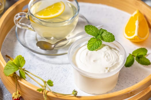 Creamy dessert with mint served on wooden tray with lemon tea, orange slice and wild strawberry twig