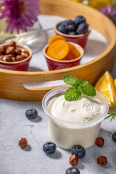 Plastic cup of creamy yogurt with mint and healthy ingredients like blueberries, hazelnuts, dried apricots and orange slices composing a delicious breakfast