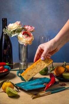 Hand placing a piece of gourmet cheese onto a plate on a table set for a romantic dinner with flowers, wine, and fruit