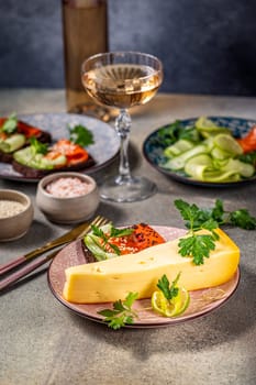 Piece of cheese, salmon canapés, cucumber salad, glass of rosé wine and seasonings compose a sophisticated appetizer platter